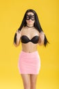 Portrait of beautiful sensual woman in black lace mask and pink skirt on yellow background. girl in venetian mask