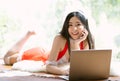 Portrait of beautiful sexy Asian woman lying on carpet with laptop computer to surf the internet with a happy relaxed smile and