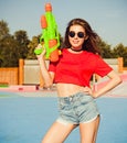 Portrait beautiful girl posing in denim shorts, white T-shirt and sunglasses in the skate park with water gun on a warm summe Royalty Free Stock Photo