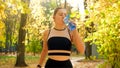 Portrait of beautiful sexy girl in sports outfit drinking water during fitness training in autumn park