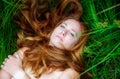 Portrait of a beautiful sexy red-haired woman, lying in the sun in happiness, relaxing on the green grass, the red hair draped Royalty Free Stock Photo