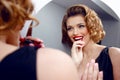 Beautiful sensual young woman applying red lipstick on lips looking at mirror. Beautiful woman makes evening makeup Royalty Free Stock Photo