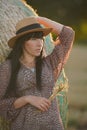 Portrait of beautiful sexy weared girl posing with haystack roll on harvested wheat field in the summer at sunset time