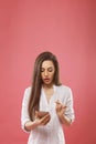 Portrait of beautiful shocked young woman posing  over pink wall background using mobile phone. Royalty Free Stock Photo