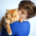 Portrait of beautiful short haired 30 years old woman in blue dress kissing her ginger red furry persian cat. Domestic animal, pet Royalty Free Stock Photo