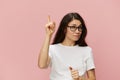 portrait of a beautiful, smart, pleasant woman in a light T-shirt and black-rimmed glasses smiling, raising her index