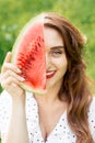 Portrait of adult girl holding slice of watermelon covering part of face. Royalty Free Stock Photo