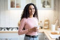 Smiling Brunette Woman With Cup Of Coffee In Hands Standing In Kitchen