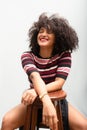 Portrait of a beautiful smiling cheerful young woman with curly hair sitting on a wooden stool Royalty Free Stock Photo