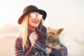 Portrait of stunning smiling hipster trendy blonde woman walking on the beach with a little dog wearing sunglasses and black hat Royalty Free Stock Photo