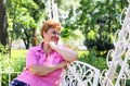 Portrait of beautiful smiling middle aged adult woman  sitting thoughtfully at white lacy bench in the park Royalty Free Stock Photo