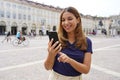 Portrait of a beautiful smiling modern girl using a mobile phone on old town square Royalty Free Stock Photo