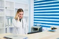 Portrait of a beautiful smiling nurse at desk station while talking on the phone and complete a medical information form Royalty Free Stock Photo