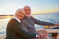 Portrait of beautiful smiling senior couple holding hands, hugging and relaxing together while sitting on the side of Royalty Free Stock Photo