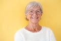 Portrait of beautiful smiling senior woman white-haired looking at camera wearing eyeglasses, isolated on yellow background Royalty Free Stock Photo