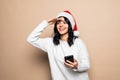 Portrait of a beautiful smiling woman christmas hat holding mobile phone while standing and looking at camera isolated over white Royalty Free Stock Photo