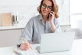 Portrait of beautiful smiling woman in glasses taking notes while speaking on mobile phone, indoors Royalty Free Stock Photo