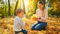 Portrait of beautiful smiling woman with little son picking up fallen yellow leaves in autumn park Royalty Free Stock Photo