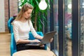 Portrait of beautiful smiling woman sitting on a comfortable chair in a cafe with black laptop. Pretty student doing work with lap Royalty Free Stock Photo