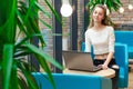 Portrait of beautiful smiling woman sitting on a comfortable chair in a cafe with black laptop. Pretty student doing work with lap Royalty Free Stock Photo