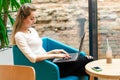 Portrait of beautiful smiling woman sitting on a comfortable chair in a cafe with black laptop. Pretty student doing work with lap Royalty Free Stock Photo