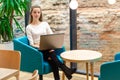 Portrait of beautiful smiling woman sitting on a comfortable chair in a cafe with black laptop. Pretty student doing work with lap Royalty Free Stock Photo