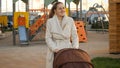 Portrait of beautiful smiling woman wlaking with baby pram on children playground Royalty Free Stock Photo