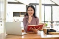 Smiling Asian female college student sits at the coffee shop with her laptop and book Royalty Free Stock Photo