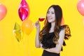 Portrait of beautiful smiling young asian woman with glass of red wine with yellow background and party balloon