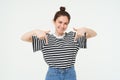 Portrait of beautiful, smiling young female model, showing advertisement, pointing fingers down, standing over white Royalty Free Stock Photo