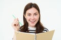 Portrait of beautiful, smiling young woman, holding pen and notebook, looking happy at camera, making notes, writing in Royalty Free Stock Photo