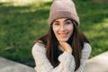 Portrait of beautiful smiling young woman looking at the camera, sitting on the bench in the city street, wearing knitted sweater Royalty Free Stock Photo
