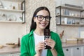 Portrait of a beautiful smiling young woman standing at home in the kitchen, holding and eating a chocolate bar in a Royalty Free Stock Photo