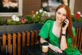 Portrait of beautiful smiling young woman talking by mobile phone, sitting at table with coffee cup in outdoor cafe Royalty Free Stock Photo