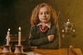 Little witch dressed in dark clothes sitting at the table against a black smoky background. There are magic wand, books Royalty Free Stock Photo