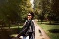 Portrait of beautiful stylish brunette girl in blue and white striped sleeveless dress and sunglasses with black leather jacket in Royalty Free Stock Photo