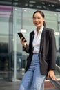 Successful Asian businesswoman holding her smartphone, standing outside of the company building Royalty Free Stock Photo