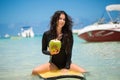 Portrait of a beautiful surfing girl with green coconut from palm tree sit on yellow surf longboard surfboard board. Royalty Free Stock Photo