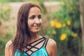 Portrait of a beautiful tanned, slender woman in a swimsuit, posing under a refreshing tropical rain. Plants and flowers on the