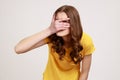 Portrait of beautiful teenager girl wearing yellow casual T-shirt spying, hiding and peeping through fingers, looking for secrets Royalty Free Stock Photo