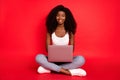 Portrait of beautiful trendy cheerful girl sitting lotus pose using laptop study learn isolated over bright red color