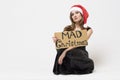 Portrait of a beautiful unhappy brunette woman in christmas hat in an elegant black festive dress holding a sign `Mad christmas ` Royalty Free Stock Photo
