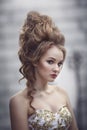 Beautiful woman in an ancient medieval dress, with a high complex historical hairstyle near the walls of the castle.