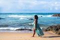 Portrait of beautiful woman with black power hair in light green long dress walking on beach sand. In the background sky clouds Royalty Free Stock Photo