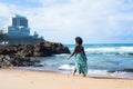 Portrait of beautiful woman with black power hair in light green long dress walking on beach sand. In the background sky clouds Royalty Free Stock Photo