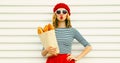 Portrait of beautiful woman blowing her red lips sending sweet air kiss holding grocery shopping paper bag with long white bread Royalty Free Stock Photo