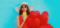 beautiful woman drinking orange juice and holding bunch of red heart shaped balloons wearing a summer straw hat, Royalty Free Stock Photo