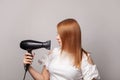 Portrait of beautiful woman drying her red hair with dryer over gray background Royalty Free Stock Photo