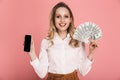 Portrait of beautiful woman holding cell phone and money fan isolated over pink background Royalty Free Stock Photo