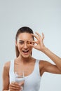 Portrait of beautiful woman holding glass of fresh water. Smiling girl taking omega 3 fish oil capsule. Royalty Free Stock Photo